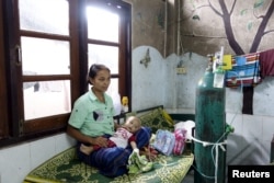 FILE - A refugee from Myanmar sits with her sick child at the Mae Tao clinic in the bordering town of Mae Sot, Oct. 30, 2015. Migrants have mixed emotions over Myanmar's election - hope that a hated government will be defeated, and fear of the uncertain future such an upheaval might bring.