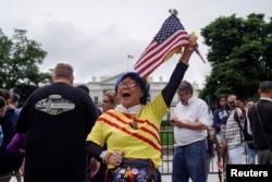 Victoria Kim, a Vietnamese Trump supporter from California, raises an American flag during a vigil outside the White House June 11, 2018, to celebrate the joint summit between U.S. President Donald Trump and North Korean leader Kim Jong Un in Singapore.