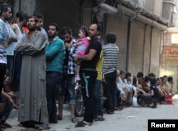FILE - People queue for bread in the rebel held al-Shaar neighborhood of Aleppo, Syria, July 14, 2016.