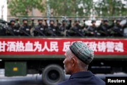 FILE - A Uighur man looks on as a truck carrying paramilitary policemen travels along a street during an anti-terrorism oath-taking rally in Urumqi, Xinjiang Uighur Autonomous Region.