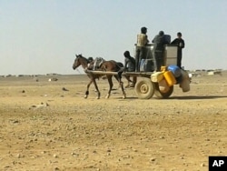 FILE - Syrian refugees ride a donkey cart full of water bottles at the Ruqban border camp, June 25, 2016.