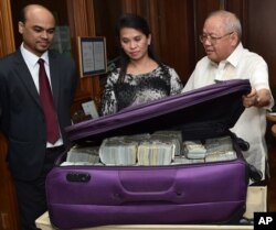 This photo provided by the Bangko Sentral ng Pilipinas, from left, Second Secretary and Head of Chancery of the Bangladesh Embassy in Manila Probash Lamarong, Anti-Money Laundering Council (AMLC) Secretariat Executive Director Julia Bacay-Abad and AMLC Member and Insurance Commissioner Emmanuel Dooc opens a bag containing US dollars that was returned by Chinese casino junket operator Kam Sin Wong to Bangladesh and Philippine AMLC officials in Manila, March 31, 2016.