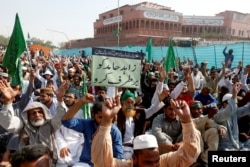 FILE - A supporter of the Tehreek-e-Labbaik Pakistan, an Islamist political party, holds a sign, which reads in Urdu, "remove Zahid Hamid" during a sit-in protest along a main road in Karachi, Pakistan, Nov. 27, 2017.