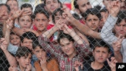 FILE - Migrants stand behind a fence at the Nizip refugee camp in Gaziantep province, southeastern Turkey, April 23, 2016. 