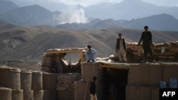 FILE - Afghan Local Police officials look on as smoke rises after an airstrike on Islamic State militant positions in a checkpoint in the eastern province of Nangarhar province, July 7, 2018.