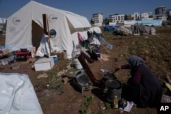 A woman cooks next a tent she and her family use as a shelter in Adiyaman, southern Turkey, Sunday, Feb. 12, 2023. (AP/Khalil Hamra)