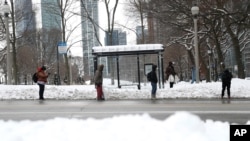 Riders wait at the bus stop on North Michigan Avenue, Feb. 16, 2021, the evening after a snow storm dumped about 18 inches of snow in the Chicago area.
