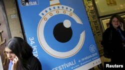 People speak on their mobile phones next to a banner of Istanbul Film Festival at the Atlas movie theater in Istanbul, Turkey, April 14, 2015. Nearly two dozen filmmakers and a group of international critics pulled out of the festival after the government prevented the screening of a film.