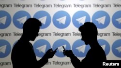 FILE - Two men pose with smartphones in front of a screen showing the Telegram logos in this picture illustration taken Nov. 18, 2015.