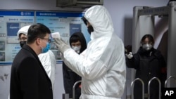 A worker wearing a hazardous materials suit takes the temperature of a passenger at the entrance to a subway station in Beijing, Jan. 26, 2020. 