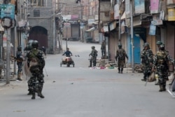 A Kashmiri municipal worker pushes a trash cart as Indian paramilitary soldiers patrol during curfew in Srinagar, India-controlled Kashmir, Aug. 6, 2019.