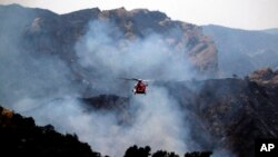 Helikopter pemadam kebakaran bersiap menjatuhkan air ke kobaran api di kawasan Pacific Palisades, Los Angeles, Minggu, 16 Mei 2021. (AP/Ringo H.W. Chiu)