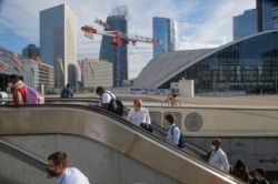 People ride an escalator as they arrive at La Defense business district while wearing a protective face masks as a precaution against the coronavirus, in Paris, Aug. 21, 2020.
