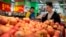 FILE - a woman wearing a uniform with the logo of an American produce company helps a customer shop for apples a supermarket in Beijing. 