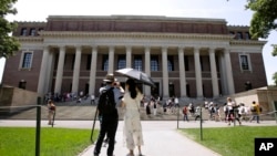 FILE - People stop to record images of Widener Library on the campus of Harvard University in Cambridge, Mass., July 16, 2019. 