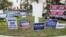 FILE - Campaign signs are posted near the Supervisor of Elections Office polling station while people line up for early voting in Pinellas County ahead of the election in Largo, Florida., Oct. 21, 2020. 
