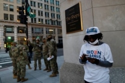 A Biden-Harris supporter stands at a corner as National Guards deploy around the city ahead of President-elect Joe Biden's inauguration ceremony, in Washington, Jan. 19, 2021.
