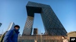 FILE- In this Feb. 4, 2021 photo, people walk in Beijing past the headquarters of Chinese state-run television network CCTV and its overseas arm CGTN, which has been stripped of its broadcasting license in Britain.