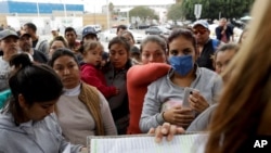 FILE - Women look on as numbers and names are called to cross the border and request asylum in the United States, in Tijuana, Mexico, Oct. 23, 2018.