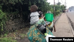 A Congolese woman carries her child and belongings as they evacuate from recurrent earth tremors as aftershocks following the eruption of Mount Nyiragongo volcano near Goma, May 27, 2021.