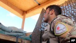 In this Oct. 7, 2019 file photo, a fighter from the U.S.-backed Kurdish-led Syrian Democratic Forces, SDF, stands guard inside a post where U.S. troops were based, in Tal Abyad town, at the Syrian-Turkish border, Syria.