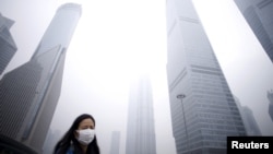 A woman wearing a mask walks past below skyscrapers amid heavy smog at the financial district of Pudong, in Shanghai, China, Dec. 11, 2015. 