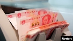 FILE - Chinese 100 yuan banknotes are seen in a counting machine while a clerk counts them at a branch of a commercial bank in Beijing, China, March 30, 2016. 