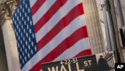 FILE - A Wall Street sign is seen against the background of a giant American flag hanging on the building of the New York Stock Exchange, in New York City, Sept. 21, 2020.