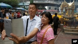 FILE - Asian tourists takes a "selfie" in front of the Erawan Shrine in Bangkok, Thailand, Oct. 22, 2015.