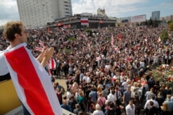 People hold old Belarusian national flags while gathered at the place where Alexander Taraikovsky died during clashes protesting election results, in Minsk, Belarus, Aug. 15, 2020.