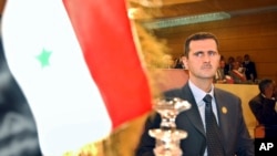 FILE - Syrian President Bashar Assad looks on at his country's flag at the opening of the 16th ordinary session of Arab Summit in Tunis, Tunisia, May 22, 2004. 