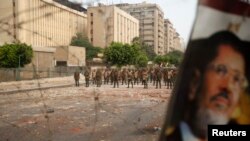 Members of the Republican Guards stand in line at a barricade blocking protesters supporting deposed Egyptian President Mohamed Morsi (pictured in poster) near a Republican Guards headquarters in Cairo, July 9, 2013./