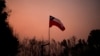 Una bandera chilena colocada en medio de árboles carbonizados bajo un cielo rojo causado por incendios forestales en Santa Juana, Chile, el 5 de febrero de 2023. 