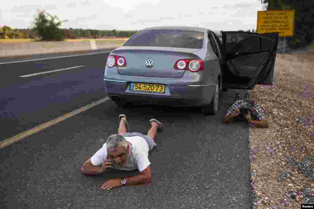Israelis take cover by the side of a road as a siren sounds a warning of incoming rockets, outside the northern Gaza Strip, July 15, 2014.