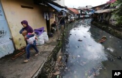A woman carrying a child walks along a garbage-strewn river at a slum in Jakarta, Indonesia, April 3, 2017. Most of Jakarta's waterways are polluted, contributing not only to a lack of clean water, but also making flooding more likely during the rainy season.