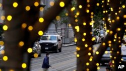 Holiday lights line trees as people wearing face masks cross an intersection during the coronavirus pandemic in San Francisco, Dec. 17, 2020. 
