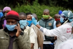 FILE - A health worker takes the temperature of a person standing in line for mass testing in an effort to stop the spread of the coronavirus disease (COVID-19) in the Kibera slum of Nairobi, Kenya, May 26, 2020.