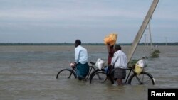 FILE - Sri Lankan men push their bicycles through flood waters after heavy rains in Batticaloa, about 320 km (199 miles) east of Colombo, Jan. 13, 2011. 