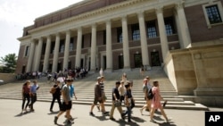 FILE - In this July 16, 2019, file photo people walk past an entrance to Widener Library, behind, on the campus of Harvard University, in Cambridge, Mass.