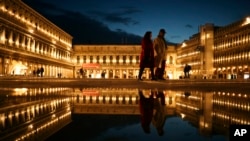FILE - Locals and tourists walk along a nearly empty St. Mark's square in Venice, Italy, March 3, 2020.