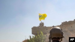 FILE - A U.S. soldier oversees members of the Syrian Democratic Forces as they demolish a Kurdish fighters' fortification and raise a Tal Abyad Military Council flag over the outpost as part of the "safe zone" near the Turkish border, Sept. 21, 2019.