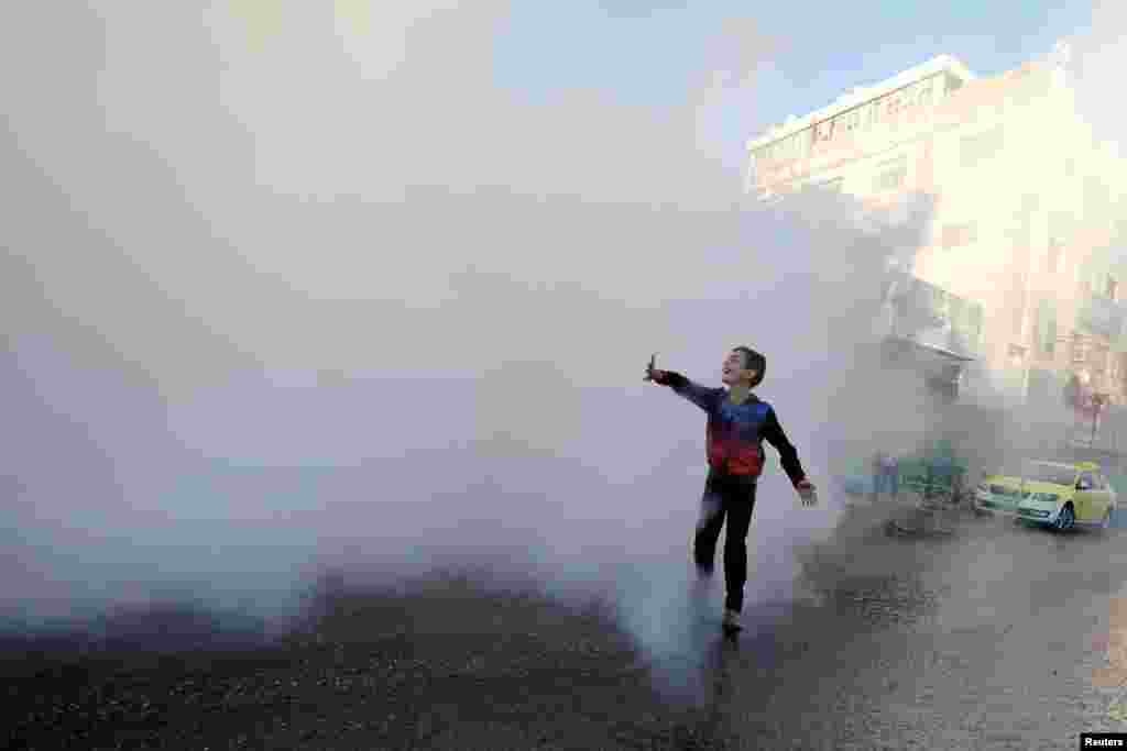 A Palestinian boy plays as disinfectants are sprayed by workers to sanitize cars and shops amid the coronavirus disease (COVID-19) outbreak in Hebron in the Israeli-occupied West Bank.