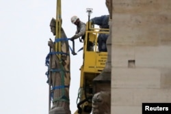 Men work on a statue on a facade at Notre-Dame Cathedral after a massive fire devastated large parts of the gothic structure in Paris, France, April 16, 2019.