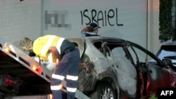 This frame grab from video provided by the Australian Broadcast Corporation Dec. 11, 2024, shows a police officer walking past a torched car being removed from in front of anti-Israel graffiti on a wall in a Sydney suburb (image partially blurred by VOA).