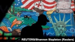 បុរសម្នាក់ពាក់ម៉ាស់ ដើរកាត់ផ្ទាំងគំនូរគូរលើជញ្ជាំងអគារមួយ ក្នុងអំឡុងការរាតត្បាតនៃជំងឺកូវីដ១៩ នៅទីក្រុងញូវយ៉ក សហរដ្ឋអាមេរិក កាលពីថ្ងៃទី៨ ខែកញ្ញា ឆ្នាំ២០២០។