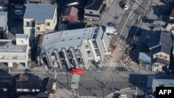 This aerial photo provided by Jiji Press shows a rescue vehicle parked next to a seven-story building that fell over in Wajima, Ishikawa prefecture on Jan. 2, 2024, a day after a major 7.5 magnitude earthquake struck Japan's Noto region.