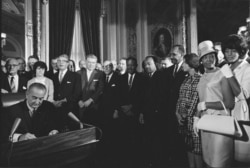 FILE - Photograph of President Lyndon Johnson signing the Voting Rights Act as Martin Luther King, Jr., with other civil rights leaders in the Capitol Rotunda, Washington, DC, Aug. 6, 1965. (Creative Commons)