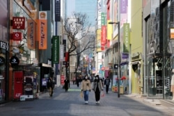 Women, wearing masks to prevent contracting the coronavirus, following the outbreak of the coronavirus disease (COVID-19), walk in a shopping district in Seoul, South Korea, March 23, 2020.