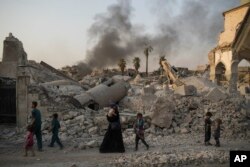 FILE - Iraqi civilians are seen walking past the destroyed al-Nuri mosque in the Old City of Mosul, Iraq, July 4, 2017.