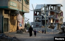 A Palestinian woman walks with her daughter as the remains of a house that witnesses said was destroyed during the 50-day war between the Hamas militant movement and Israel, in the east of Gaza City, Oct. 12, 2014.